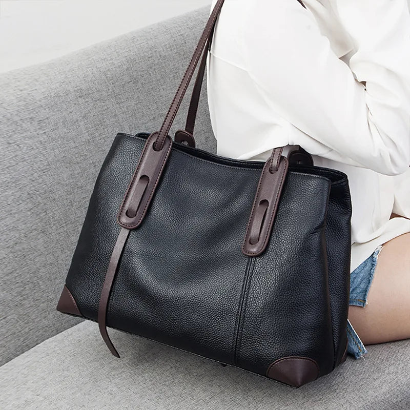 Black leather handbag with brown accents on a gray surface