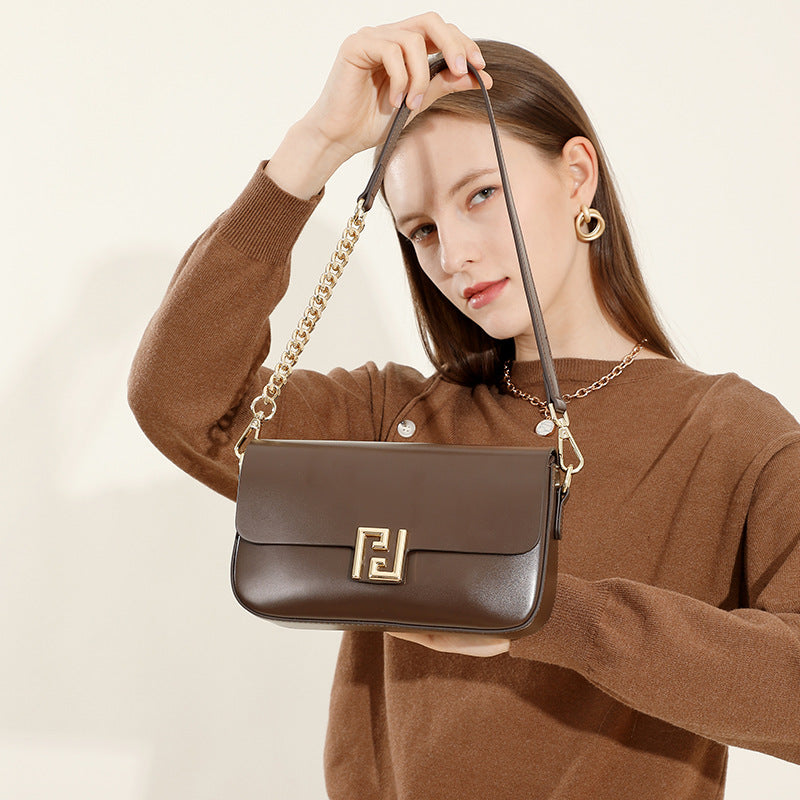 Woman holding a brown handbag with a gold chain strap against a beige background