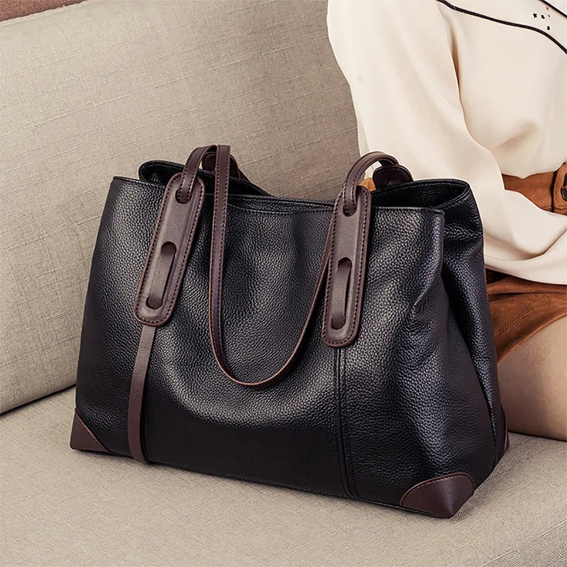 Black leather handbag with brown handles and trim on a light gray surface.