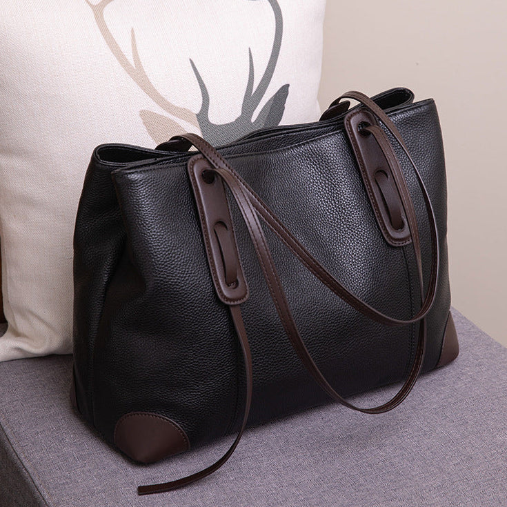 Black leather handbag with brown accents on a gray surface