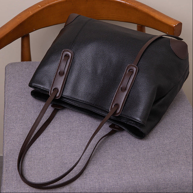 Black leather handbag with brown straps on a gray chair