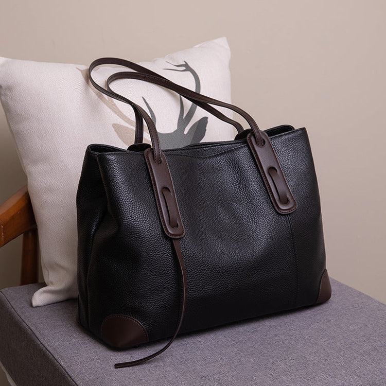 Black leather handbag with brown accents on a chair